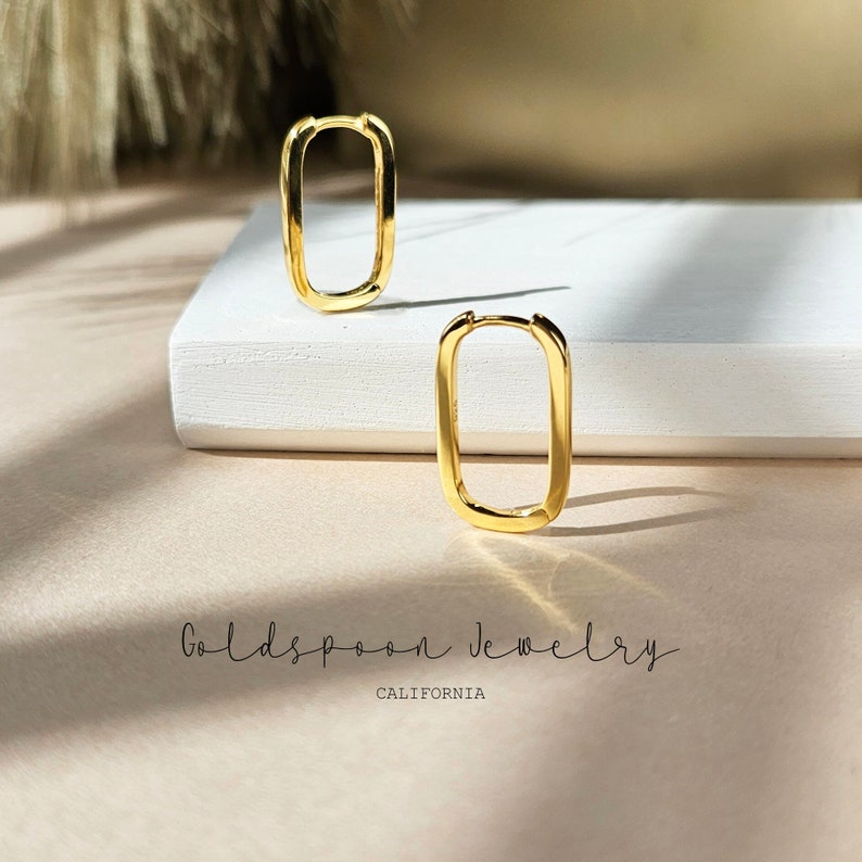 K&ouml;nnte beinhalten: Ein Paar goldene rechteckige Creolen auf einer wei&szlig;en Oberfl&auml;che. Die Ohrringe sind schlicht und modern im Design. Goldspoon Jewelry California.