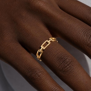 May include: A gold-toned ring featuring a continuous chain-link design. The band is composed of small, rectangular, interlocking metal links that form a uniform, repeating pattern around the entire circumference of the circular jewelry piece.