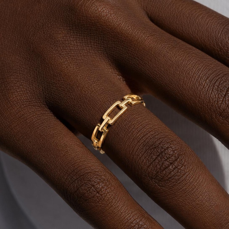 May include: A gold-toned ring featuring a continuous chain-link design. The band is composed of small, rectangular, interlocking metal links that form a uniform, repeating pattern around the entire circumference of the circular jewelry piece.