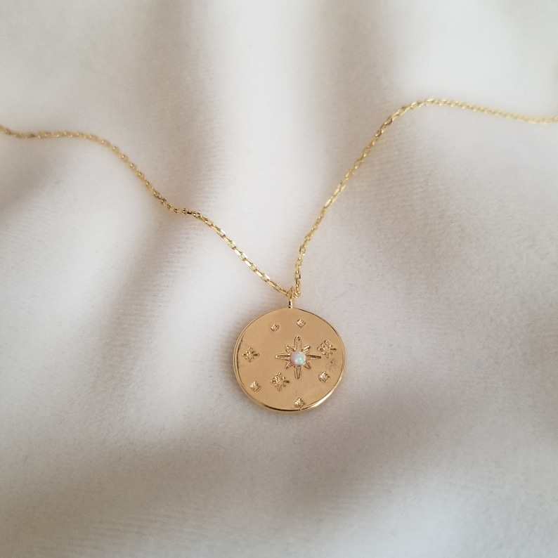 May include: Gold necklace with a round pendant featuring a starburst design with a white opal in the center. The pendant is surrounded by smaller stars.