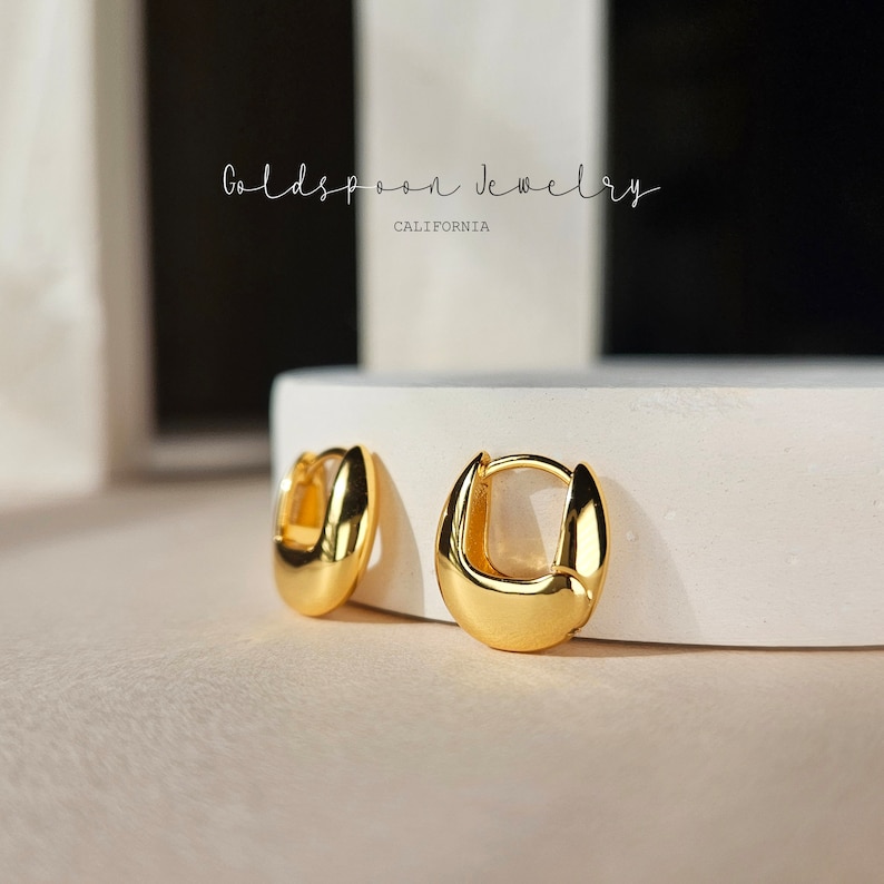 May include: A pair of gold hoop earrings on a white surface. The earrings are simple and elegant, with a smooth, polished finish.