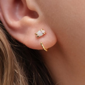 Puede incluir: Un pendiente de oro con un &oacute;palo de talla marquesa engastado en cuatro garras, situado sobre un peque&ntilde;o aro de oro liso que rodea la parte inferior del l&oacute;bulo de la oreja, creando un aspecto superpuesto con un acabado met&aacute;lico pulido.