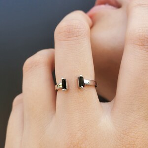 May include: A silver ring with two black rectangular stones. The ring is open on one side and has a simple design.
