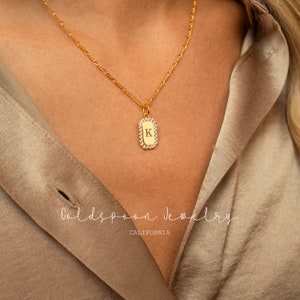 Op de afbeelding: Een gouden ketting met een klein rechthoekig hangertje met een enkele letter 'K' omringd door heldere zirkonia-stenen. Het hangertje is gedragen door een model dat een beige shirt draagt. De tekst 'Goldspoon Jewelry CALIFORNIA' is zichtbaar onderaan de afbeelding.
