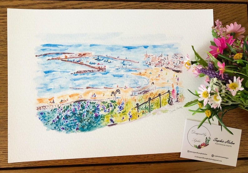 Może przedstawiać: Akwarela przedstawiająca scenę na plaży z błękitnym morzem, piaszczystym brzegiem i budynkami w tle. Grafika zawiera czarną balustradę, kwiaty i napis "Designed by Sophie Helen".
