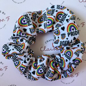 May include: White scrunchie with a rainbow and heart print and the word "PRIDE" repeated throughout.