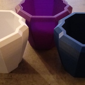 May include: Three geometrically shaped planters, one white, one purple, and one blue.