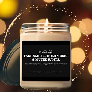 Può includere: Una candela accesa in un barattolo di vetro con un'etichetta nera. L'etichetta recita "smells like FAKE SMILES, HOLD MUSIC & MUTED RANTS." Sotto c'è la citazione: "Your call is very important... to my paycheck" - Customer Service Rep.