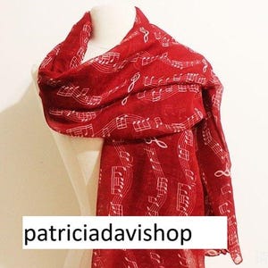 May include: A red scarf with a white musical note pattern is draped over a mannequin. The scarf is made of a lightweight material and features the text "patriciadavishop".