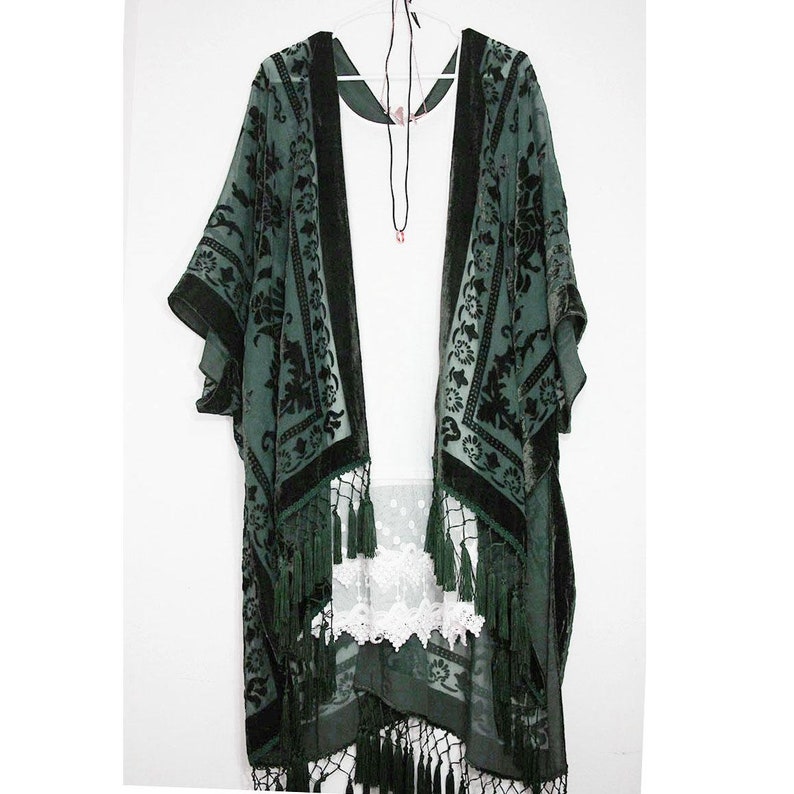 K&ouml;nnte beinhalten: Ein dunkelgr&uuml;nes Samt-Kimono mit schwarzen Blumenstickereien und Fransenbesatz. Das Kimono ist durchsichtig und hat eine lockere Passform.