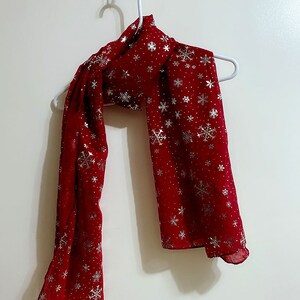 Puede incluir: Una bufanda roja con un patr&oacute;n de copo de nieve plateado.