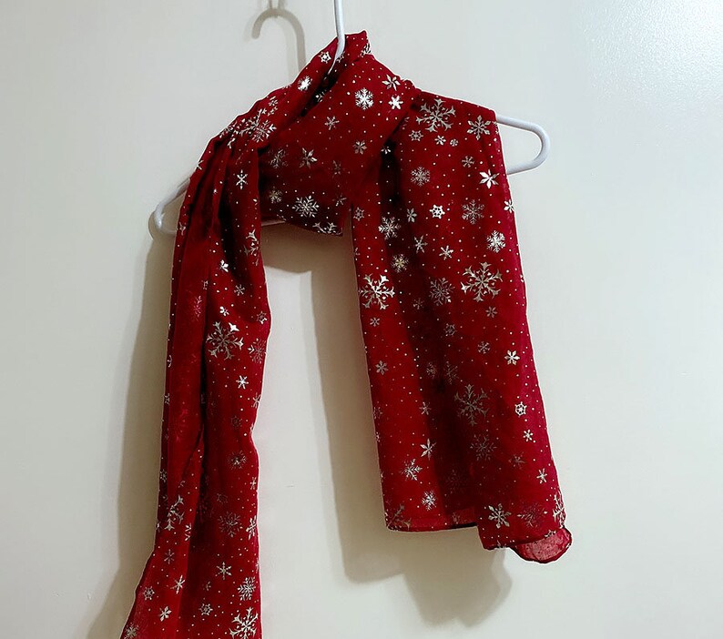 Puede incluir: Una bufanda roja con un patr&oacute;n de copo de nieve plateado.