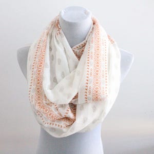 May include: A white infinity scarf with a brown and white geometric pattern. The scarf is made of a soft, lightweight fabric and is perfect for adding a touch of style to any outfit.