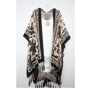 May include: A black and beige kimono with a floral pattern and fringe trim. The kimono is made of a lightweight fabric and has a relaxed fit.