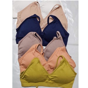 Könnte beinhalten: Fünf nahtlose BHs in verschiedenen Farben: Beige, Marineblau, Hellbraun, Pfirsich und Gelb. Die BHs haben einen V-Ausschnitt und verstellbare Träger.