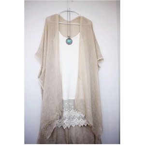 May include: A beige sheer kimono with a white lace trim and a silver necklace with a turquoise stone pendant.