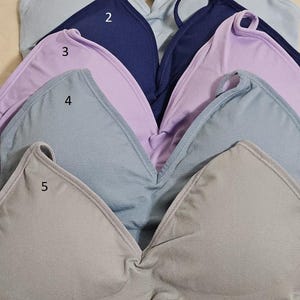 May include: Five seamless bras in different colors, including light blue, lavender, gray, and beige. The bras are stacked on top of each other, with the straps visible. The text "SIZE REGULAR" is printed on the top of the image.