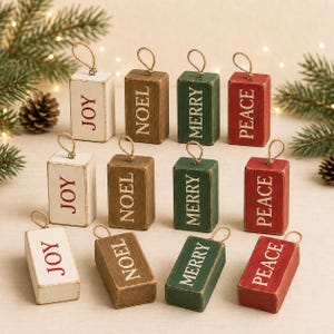 May include: Twelve rectangular wooden block ornaments with jute twine loops. The blocks are painted white, brown, green, or red, each featuring the word JOY, NOEL, MERRY, or PEACE in white or red capital letters with a distressed finish.