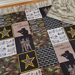 May include: A camouflage fabric quilt with a black background and yellow stars. The quilt has a variety of patches with text that reads "ARTILLERY HOOAH COMBAT ENGINEER AIRBORN DIVISION INFANTRY HUA INFAN NE SECOND TO NONE" and "FIRST IN LAST OUT".