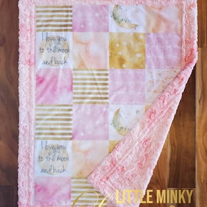 May include: A pink and gold baby blanket with a patchwork design featuring moons, stars, and the text "I love you to the moon and back". The blanket is trimmed with a fluffy pink border and has the text "Little Minky Luxuries" in gold lettering.