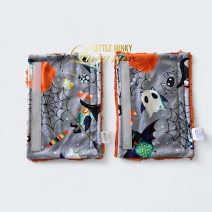 May include: Two gray Halloween-themed fabric items with orange trim and velcro closures. The fabric features a spiderweb design with bats, ghosts, owls, and pumpkins. The text "Little Minky Luxuries" is visible in the image.