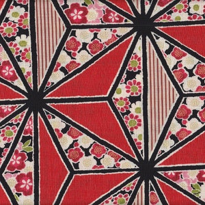 May include: Geometric fabric pattern featuring red, black, and white shapes. The design includes red triangles, black outlines, and floral patterns with pink, white, and green flowers. A striped section adds detail.