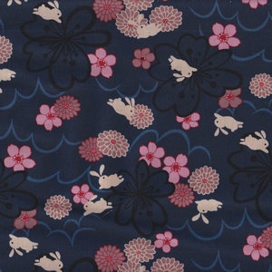 May include: A navy blue fabric with a repeating pattern of white rabbits, pink cherry blossoms, and dark gray stylized flowers. The background is a dark blue with a wavy pattern.