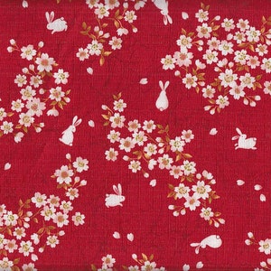 May include: Red fabric with a repeating pattern of white rabbits and white cherry blossoms with gold accents.