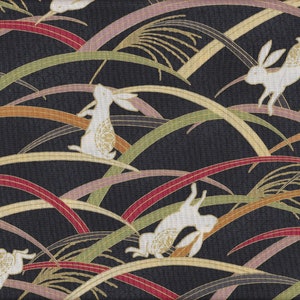 Könnte beinhalten: Ein sich wiederholendes Muster mit weißen Kaninchen mit goldenen Akzenten, die über einen schwarzen Hintergrund springen. Das Design umfasst geschwungene Linien in Rot, Grün, Gold und Lila, die stilisiertem Gras ähneln.