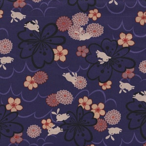 Könnte beinhalten: Dunkelblauer Stoff mit einem sich wiederholenden Muster aus weißen Kaninchen, Blumen mit schwarzem Zentrum und rosa und pfirsichfarbenen Blüten. Das Design umfasst stilisierte wellenartige Linien.