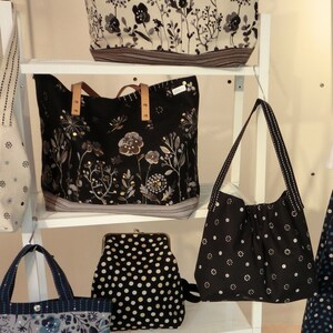 May include: A display of tote bags and purses with floral patterns in black, white, and grey. Some have leather handles. One purse is black with white polka dots. The bags are on white shelves.