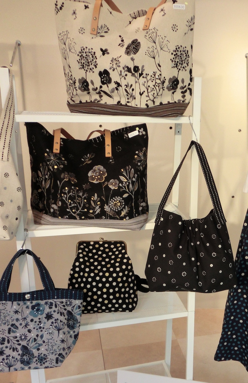 May include: A display of tote bags and purses with floral patterns in black, white, and grey. Some have leather handles. One purse is black with white polka dots. The bags are on white shelves.