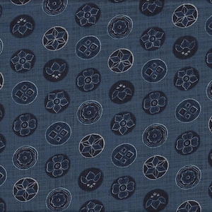 May include: Close-up of a blue fabric with a repeating pattern of navy blue and white floral and geometric designs within oval shapes. The fabric has a textured appearance.