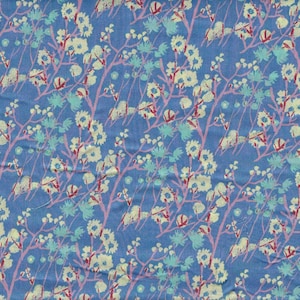 May include: A blue fabric with a repeating floral pattern. The design features white flowers, light blue accents, and pink branches. The fabric has a slightly textured appearance.