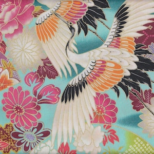 Op de afbeelding: Een turquoise stof met een herhalend patroon van witte kranen met zwarte en oranje accenten, roze en witte bloemen en gouden accenten.