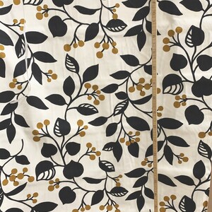 May include: Cream-colored fabric with a repeating pattern of black leaves and golden-brown berries. A wooden ruler is placed vertically along the fabric, showing measurements in inches. The design is suitable for home decor or apparel.
