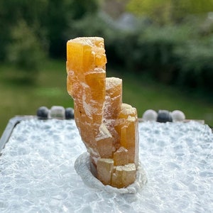 May include: A yellow-brown crystal specimen with a layered, stacked structure, displayed in a black and white foam-lined box.