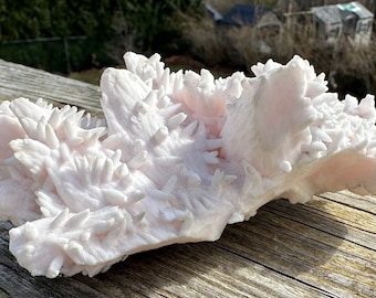May include: A large, pink, spiky crystal cluster. The crystal is a natural formation with a rough, textured surface.