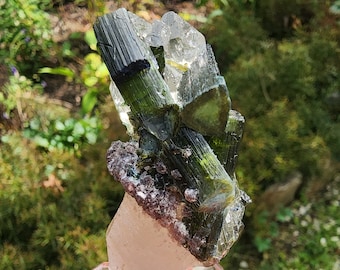 May include: A cluster of green and black tourmaline crystals on a clear quartz point, mounted on a clear acrylic base.