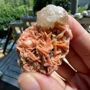 K&ouml;nnte beinhalten: Ein Cluster aus rosa und wei&szlig;en Kristallen. Die rosa Kristalle sind in einem zarten, geschichteten Muster angeordnet, w&auml;hrend der wei&szlig;e Kristall obenauf sitzt. Die Kristalle sind durchscheinend und haben einen leichten Schimmer.
