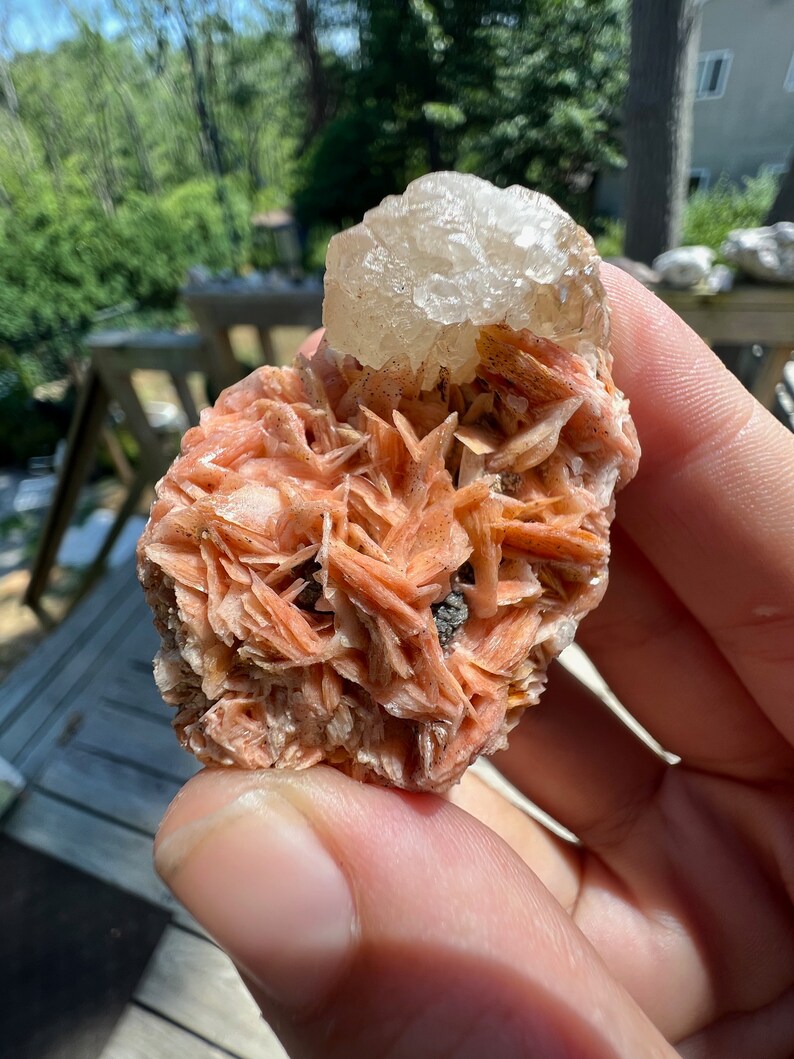 K&ouml;nnte beinhalten: Ein Cluster aus rosa und wei&szlig;en Kristallen. Die rosa Kristalle sind in einem zarten, geschichteten Muster angeordnet, w&auml;hrend der wei&szlig;e Kristall obenauf sitzt. Die Kristalle sind durchscheinend und haben einen leichten Schimmer.