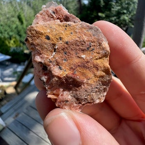 K&ouml;nnte beinhalten: Ein rosa-brauner Baryt-Kristall mit schwarzen Einschl&uuml;ssen. Der Kristall ist rau und hat ein nat&uuml;rliches, unpoliertes Aussehen.