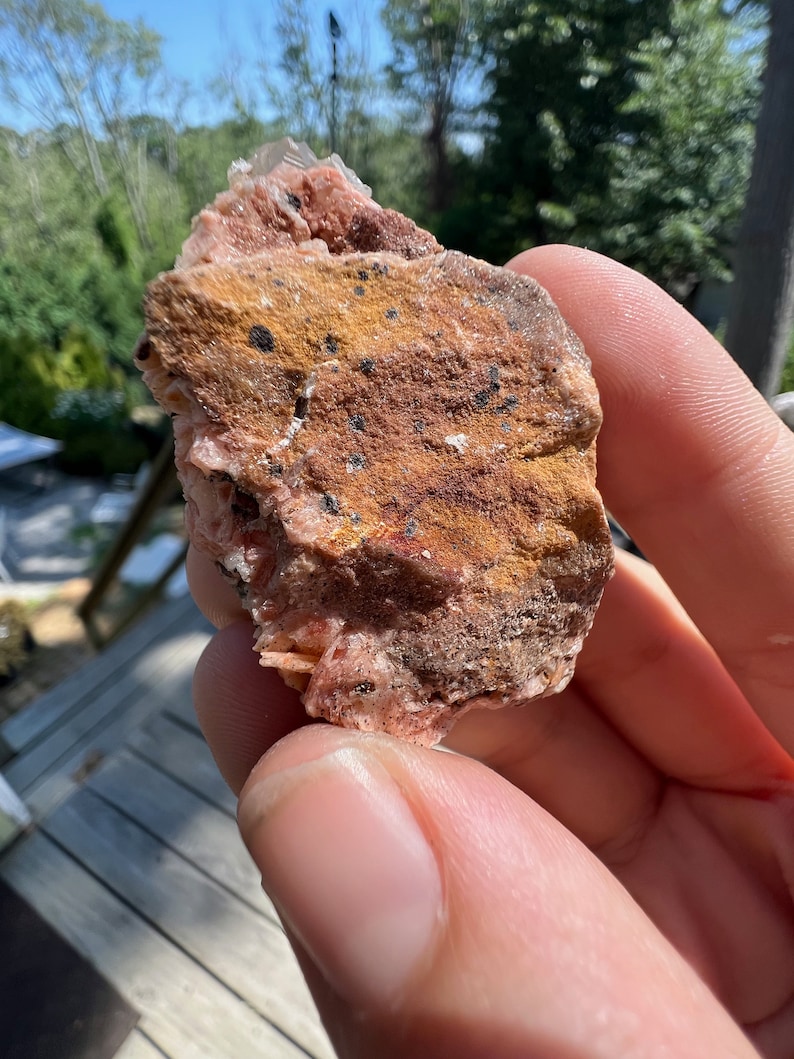 K&ouml;nnte beinhalten: Ein rosa-brauner Baryt-Kristall mit schwarzen Einschl&uuml;ssen. Der Kristall ist rau und hat ein nat&uuml;rliches, unpoliertes Aussehen.