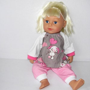 Könnte beinhalten: Eine blonde Puppe, die ein graues und rosa Outfit mit einem weißen Langarmshirt trägt. Das Outfit zeigt einen niedlichen Cartoon-Hund mit einem herzförmigen Ballon.