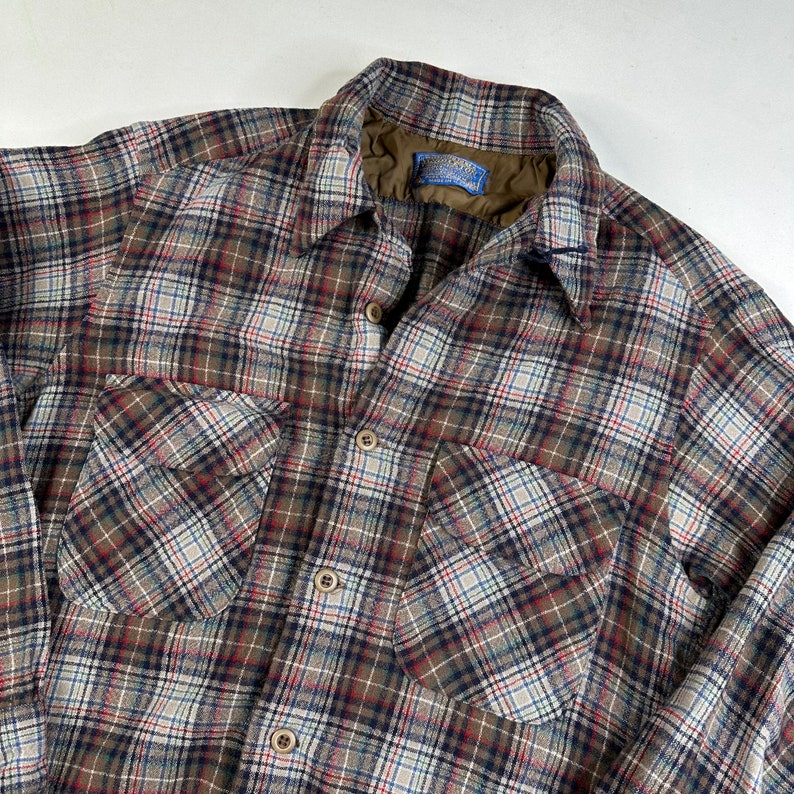 May include: A brown, white, and blue plaid flannel shirt with a button-up front and two chest pockets. The shirt has a label that reads "Pendleton."