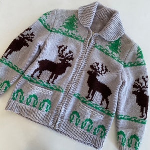 May include: A gray knitted cardigan with a zipper closure and a pattern of brown reindeer and green trees. The cardigan has two pockets.