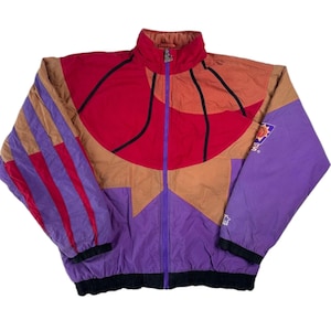 Könnte beinhalten: Eine violette, rote und braune Vintage-Basketballjacke mit Reißverschluss und einem Teamlogo auf dem rechten Ärmel. Die Jacke hat ein geometrisches Design mit einem Basketballmuster.