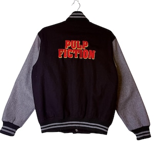 May include: Black varsity jacket with gray sleeves. The back of the jacket features the words "PULP FICTION" in red and gold lettering. The jacket has a striped collar, cuffs, and hem.