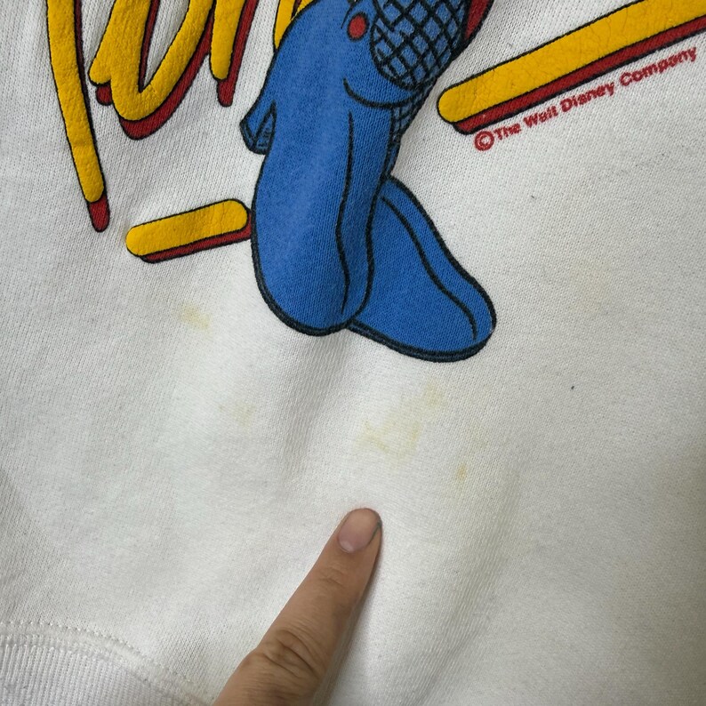 Puede incluir: Sudadera blanca con un personaje de dibujos animados en azul, rojo y amarillo. La palabra "Run" est&aacute; en amarillo con un contorno rojo. Se ve el copyright de The Walt Disney Company. La sudadera tiene algunas manchas amarillas.