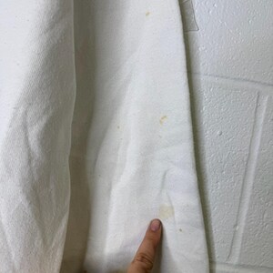 Puede incluir: Primer plano de una tela blanca con varias manchas amarillas. La tela parece ser una secci&oacute;n de una prenda, posiblemente una camisa o sudadera. La textura de la tela es visible y las manchas se concentran en varias &aacute;reas.